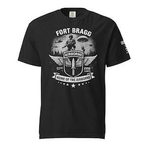 May include: Black t-shirt with a distressed graphic featuring the text "FORT BRAGG" and "HOME OF THE AIRBORNE." The design includes an image of a soldier, a parachute, wings, and the text "82ND XVIII CORPS."