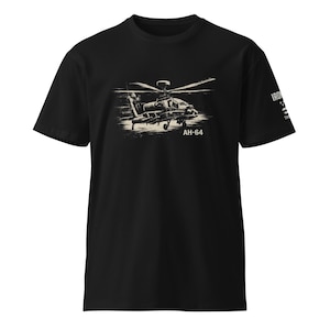 Könnte beinhalten: Schwarzes T-Shirt mit einer Illustration im Vintage-Stil eines AH-64 Apache Hubschraubers. Das Design enthält den Text "AH-64" unter dem Flugzeug. Das T-Shirt hat kurze Ärmel und einen Rundhalsausschnitt.