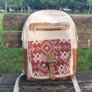 Peut inclure: Un sac à dos en toile beige avec un rabat en cuir marron et un motif géométrique sur le devant. Le sac à dos a une fermeture éclair et une boucle.