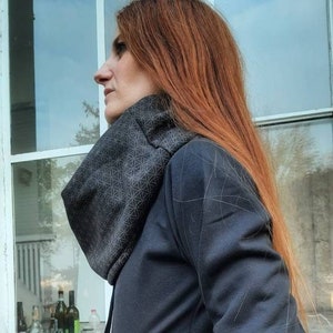 Könnte beinhalten: Dunkelgraue Kapuzenjacke mit geometrisch gemusterten Ärmeln und Kragen. Die Jacke hat einen Reißverschluss und einen Knopf. Die Ärmel und der Kragen weisen ein sich wiederholendes geometrisches Design in Hellgrau auf.