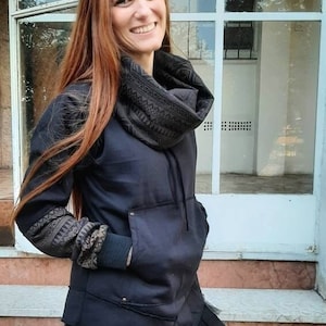 Può includere: Una felpa con cappuccio nera con un collo a scialle con motivo geometrico e una gonna di tulle nera. La felpa ha una grande tasca sul davanti e un cappuccio con coulisse.