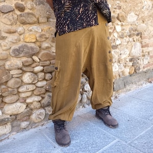 Può includere: Pantaloni harem color senape con chiusura a bottoni e tasca cargo. I pantaloni sono abbinati a stivali marroni e una camicia nera fantasia. I pantaloni hanno una vestibilità ampia e sono realizzati in tessuto morbido.