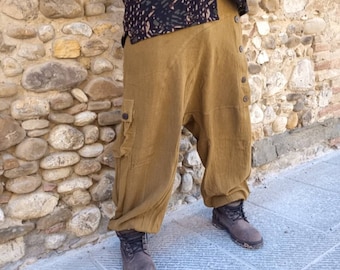 May include: Mustard-colored harem pants with a button closure and a cargo pocket. The pants are paired with brown boots and a black patterned shirt. The pants have a relaxed fit and are made of a soft fabric.