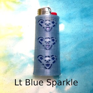 May include: A light blue lighter with a sparkle finish and a design of three bears on the side.  The lighter is labeled "Lt Blue Sparkle".