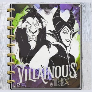May include: A planner featuring illustrations of Scar and Maleficent with the text "Villainous Vibes." The cover has a colorful abstract background with green, purple, and white ink-like designs. The planner is bound with gold-colored rings.