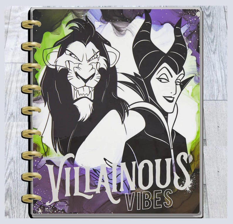 May include: A planner featuring illustrations of Scar and Maleficent with the text "Villainous Vibes." The cover has a colorful abstract background with green, purple, and white ink-like designs. The planner is bound with gold-colored rings.