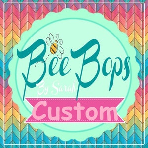 Puede incluir: Logotipo de "Bee Bops By Sarah Custom" con letras en cursiva turquesa y una abeja de dibujos animados. El logotipo está sobre un círculo festoneado verde claro, con una pancarta rosa que dice "Custom". El fondo tiene un patrón de chevrón colorido.