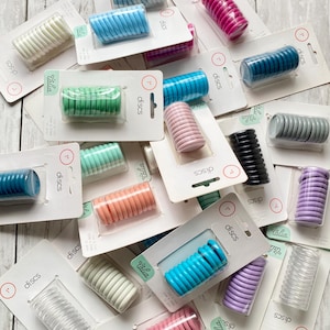 May include: An assortment of colorful 1-inch discs in various hues, including pink, blue, green, and clear, are displayed on white packaging. The discs are spiral-shaped and are designed for use in notebooks or planners.