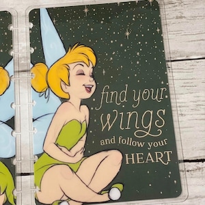 May include: A clear, rectangular planner insert featuring a cartoon fairy in a green dress and yellow hair. The text "find your wings and follow your HEART" is written on a dark green background with white stars.