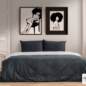 Pu&ograve; includere: Due stampe in bianco e nero di donne con acconciature afro, realizzate con linee. Le stampe sono incorniciate con cornici nere e sono appese a un muro bianco sopra un letto grigio.