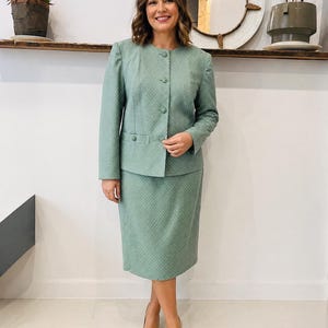 May include: A light green skirt suit with a dotted pattern. The suit features a button-up jacket and a knee-length skirt. The person is wearing beige heels.