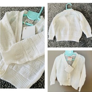 May include: White knitted cardigan with a button closure. The cardigan has a textured pattern and is shown on a hanger.