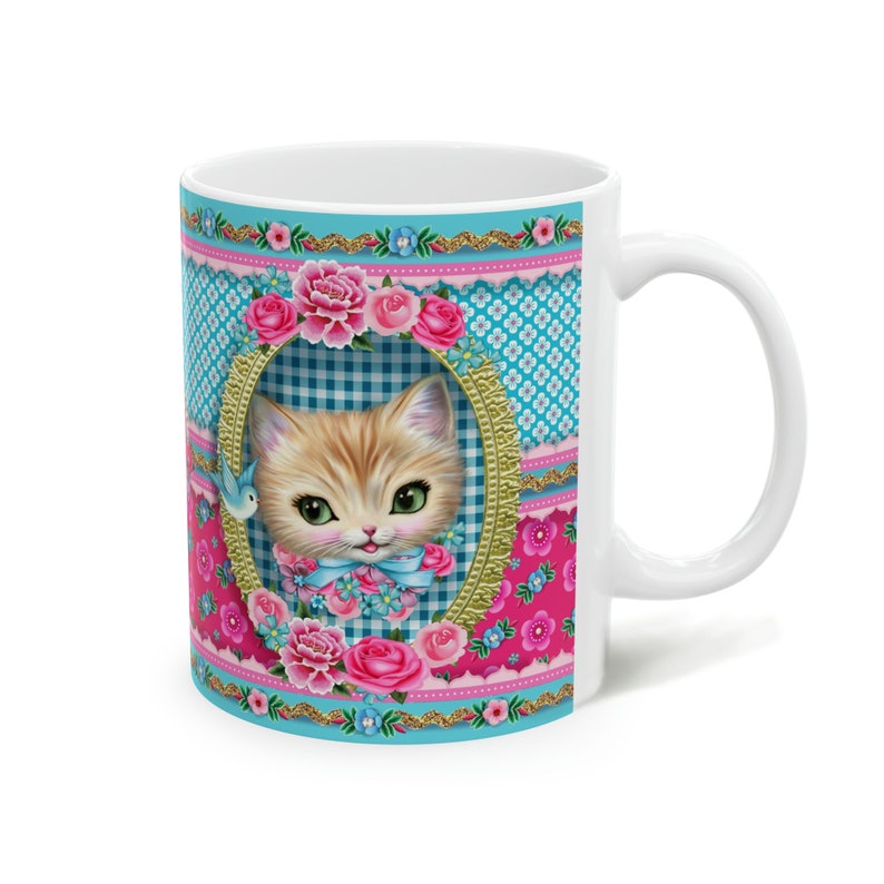 May include: White ceramic mug with a colorful design featuring a kitten with blue eyes, pink flowers, and a blue bird. The background is a patchwork of blue and pink gingham patterns.