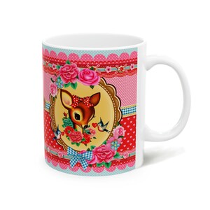 May include: White ceramic mug with a colorful design featuring a cartoon deer with a red bow, surrounded by pink and red flowers and blue birds. The background is a pink and red polka dot pattern with white lace trim.