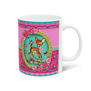 May include: White ceramic mug with a pink, teal, and white floral design featuring a cartoon fawn in a gold frame. The fawn is surrounded by flowers and butterflies.