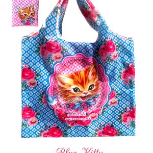 Puede incluir: Bolso tote azul con dise&ntilde;o floral y gatito. El bolso presenta un fondo azul con un patr&oacute;n floral blanco repetido y rosas rosas. Un gran gato atigrado naranja est&aacute; centrado en el bolso, rodeado por un marco rosa y las palabras "kittens are my happy place."