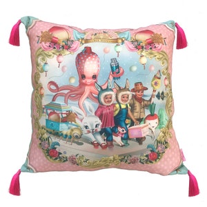 May include: Square cushion with a whimsical illustration featuring an octopus, children in bunny hats, and a white rabbit. The cushion has a pink background with a floral and polka dot pattern, gold trim, and pink tassels at each corner.