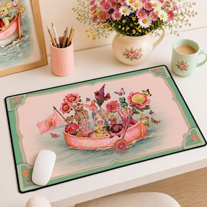 May include: A rectangular desk mat featuring a pink illustration of anthropomorphic animals in a boat, surrounded by flowers and butterflies. The border is light green with decorative corners. A white computer mouse rests on the mat surface.