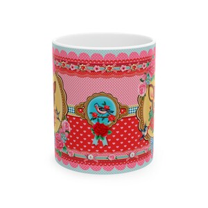 May include: A white ceramic mug with a colorful design featuring pink, red, blue, and yellow. The design includes birds, flowers, hearts, and polka dots.