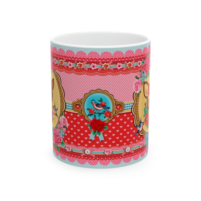 May include: A white ceramic mug with a colorful design featuring pink, red, blue, and yellow. The design includes birds, flowers, hearts, and polka dots.