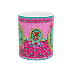 May include: A pink and turquoise ceramic mug with a floral pattern and a deer design. The mug has the words "Sweet Heart" on it.