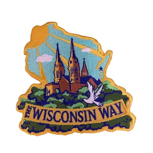 Op de afbeelding: Geborduurde patch met een gele omtrek van de staat Wisconsin met een kerkgebouw, een duif en de tekst "The Wisconsin Way".