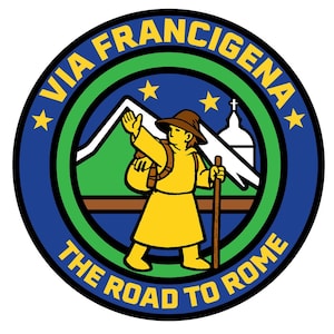 Op de afbeelding: Rond embleem met de tekst "VIA FRANCIGENA" in geel en "THE ROAD TO ROME" in wit. Het ontwerp toont een pelgrim met een rugzak en staf, bergen, sterren en een kerk, allemaal in een blauw, groen en geel kleurenschema.