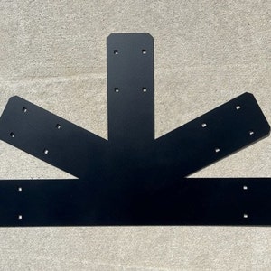 May include: Black metal brace with multiple holes for attaching to wood. The brace is shaped like a three-pointed star.