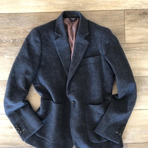 May include: A dark gray blazer with a notched lapel, two front pockets, and three buttons on each cuff. The blazer has a single-button closure and a brown interior lining. The jacket is made of a textured fabric.