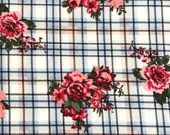 Op de afbeelding: Witte stof met een blauw en perzikkleurig ruitpatroon en een bloemenprint met roze en rode rozen.