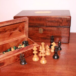 May include: A wooden chess set with black and white pieces in a wooden box. The box is open and the pieces are scattered on a wooden table.