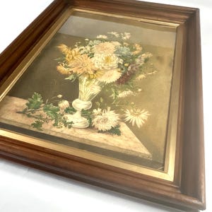 May include: A framed vintage still life print of a bouquet of white, yellow, and pink flowers in a white vase on a marble table.