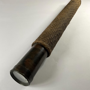 May include: A vintage brass telescope with a woven brown leather grip. The telescope has a lens at one end and a dark brown finish. The design is reminiscent of antique nautical instruments.