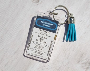 May include: A clear plastic keychain with a blue tassel. The keychain has a Fastpass ticket for Spaceship Earth at Walt Disney World. The ticket is valid for return anytime between 9:10 PM and 10:00 PM on Friday, October 1, 1982.