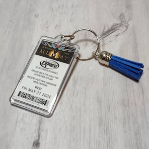 May include: A clear plastic keychain with a blue tassel. The keychain features a pass for the Revenge of the Mummy ride at Universal Studios. The pass is valid for Friday, May 21, 2004.