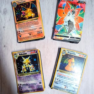 May include: Four rectangular wallets featuring graphic prints of trading cards. The top left wallet displays a Charizard, the top right shows Volcarona V, the bottom left features Alakazam, and the bottom right depicts a Dragonite character design.