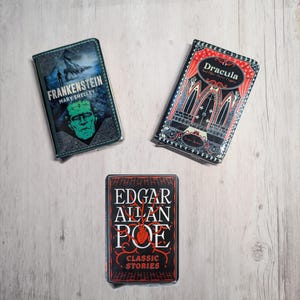 May include: Three book-themed phone cases. One case features the title "Frankenstein" by Mary Shelley, with a green monster graphic. Another case displays "Dracula" with gothic illustrations. The third case shows "Edgar Allan Poe: Classic Stories".