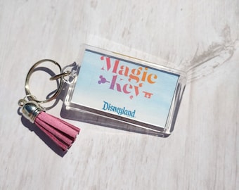 May include: A clear plastic keychain with a pink tassel. The keychain features a colorful graphic that says "Magic Key" with a Mickey Mouse icon and the text "Disneyland".
