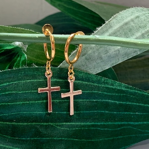 May include: A pair of gold hoop earrings with a small gold cross charm hanging from each hoop.
