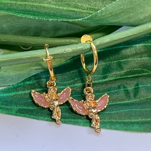 May include: A pair of gold hoop earrings with a pink angel charm dangling from each hoop.