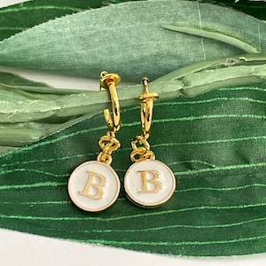 May include: A pair of gold hoop earrings with a white enamel charm featuring the letter "B" in gold.