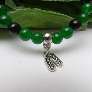May include: A green and black beaded bracelet with a silver charm of two ballet shoes.
