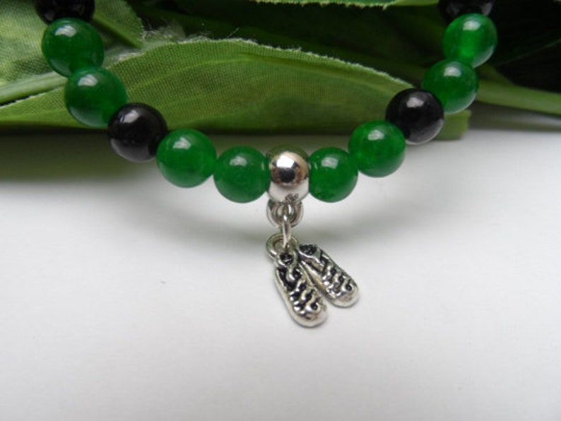 May include: A green and black beaded bracelet with a silver charm of two ballet shoes.