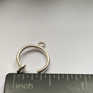 May include: Silver ring charm with a small loop at the top and a flat, round base. The ring is about 1 inch in diameter.