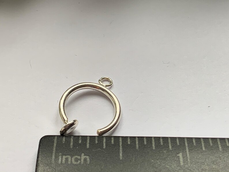 May include: Silver ring charm with a small loop at the top and a flat, round base. The ring is about 1 inch in diameter.