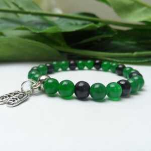 May include: A green and black beaded bracelet with a silver charm. The charm is shaped like two small shoes.