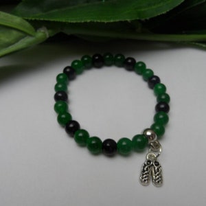 May include: A green and black beaded bracelet with a silver charm of two shoes.