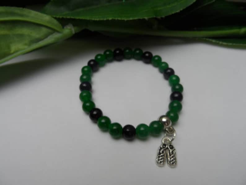 May include: A green and black beaded bracelet with a silver charm of two shoes.