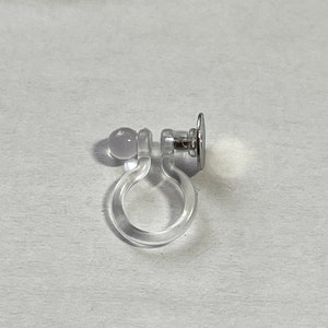 Op de afbeelding: Een doorzichtige plastic oorbel achterkant met een zilveren metalen pen en een doorzichtige plastic bal.
