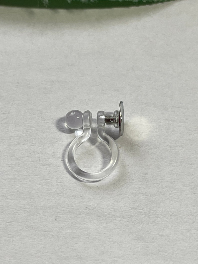 Op de afbeelding: Een doorzichtige plastic oorbel achterkant met een zilveren metalen pen en een doorzichtige plastic bal.